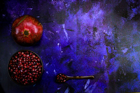 Full wooden bowl with pomegranate seeds with wooden spoon next to which there are pomegranate seeds. Whole ripe pomegranate. Bowl full of seeds with a spoonful of seeds on blue background. Copy text.の写真素材