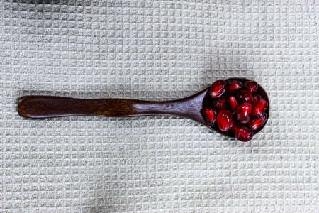 Close up of pomegranate seeds on a wooden spoon. A wooden spoon with red ripe pomegranate seeds on a linen napkin. Macro of pomegranate seeds on a wooden spoon.の写真素材