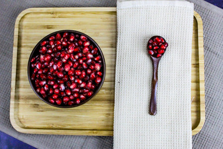 Red pomegranate seeds in a wooden bowl with a wooden spoon with the seeds next to the napkin. Red pomegranate seeds served on a wooden tray.の写真素材