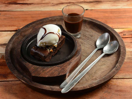 sizzling chocolate brownie is a sweet dish made using scoop of ice-cream on top served with a generous pouring of melted chocolate syrup on wooden plate. server hot. selective focusの写真素材