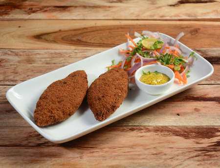 tasty crispy fried fish cutlets served with chutney, lemon,carrot and onions on a rustic wooden...