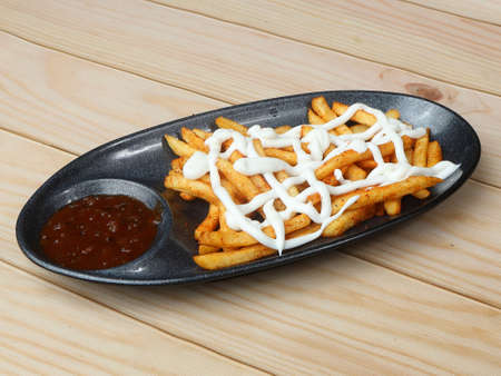 Mayo French fries topped with mayonnaise, served in a plate with tomato ketchup over a rustic wooden...