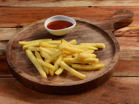 Golden fried French fries tomato ketchup served in a wooden board with over a rustic wooden...