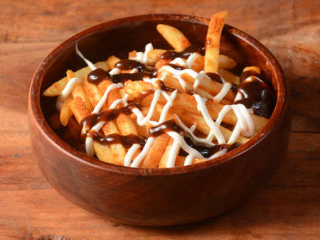 French fries topped with barbeque sauce and mayonnaise served in a wooden bowl over a rustic wooden background, selective focusの写真素材
