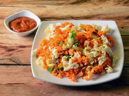 Tasty Schezwan Egg fried rice with tomato sauce served in white plate over a rustic wooden background, Indian cuisine, selective focusの写真素材
