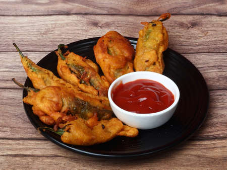 Mirchi pakora or Mirchi bhajji served with sauce, a famous midday snack in india, served over a rustic wooden background, selective focusの写真素材
