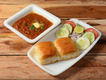 Pav Bhaji is a fast food dish from India, Thick and spicy vegetable curry, served with a soft bread roll or Bun Paav and butter. isolated over a rustic wooden background, selective focusの写真素材
