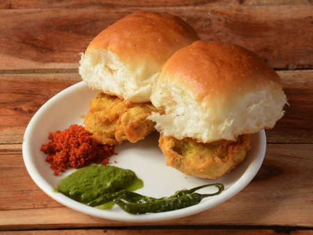 Vada Pav, Mumbai Famous vada paav is an indian burger. Potato patty is deep fried and stuffed inside a paav or bun like burger, served over a rustic wooden background, selective focusの写真素材