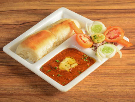 Pav Bhaji is a fast food dish from India, Thick and spicy vegetable curry, served with a soft bread roll or Bun Paav and butter. isolated over a rustic wooden background, selective focusの写真素材