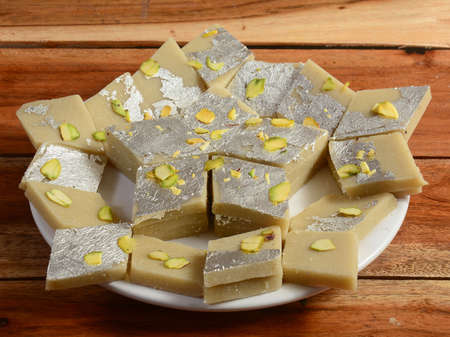 Kaju katli traditional indian sweet,served over a white plate on a rustic wooden background,...