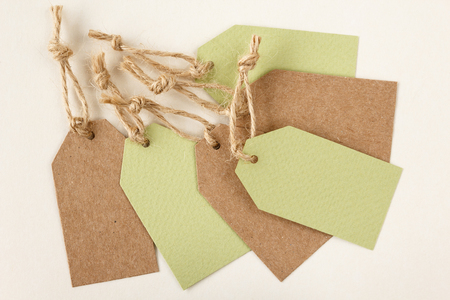 Set of blank, light green and brown rough cardboard price tags tied with jute twine on light beige backgroundの写真素材