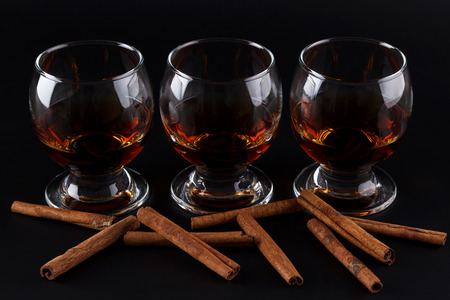 Three glasses with cognac on a black background with scattered cinnamon sticksの写真素材