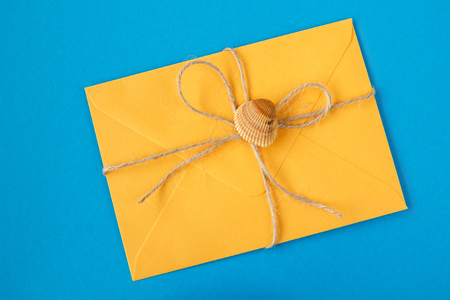 Amber yellow colored greeting envelope tied with jute twine and seashell on a blue background