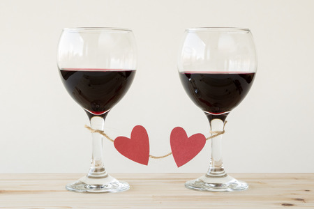 Two glasses of red wine, tied with jute twine and red hearts, on a wooden table against beige background. Celebrating loveの写真素材