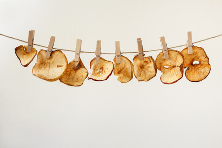 Dried apple slices hanging on a jute twine with wooden clothespins. Drying fruits at home. Space for textの写真素材