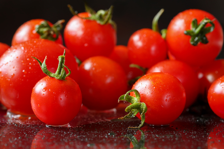 Extreme close up of fresh, organic cherry tomatoes on a black reflective background with waterdrops. Selective focus and shallow depth of fieldの写真素材