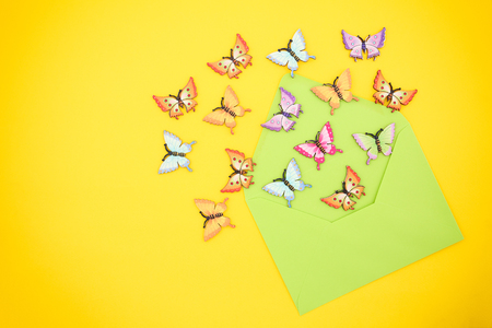 Top view of decorative, multicolored butterflies flying out of an open, green envelope from recycled paper on a vibrant yellow background. Hello Summer concept. Space for text.の写真素材