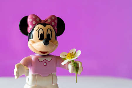 New York, USA - May 25, 2021: A close up shot of a miniature famous Disney character Minnie Mouse Disney character holding a flower against a pink background.のeditorial素材