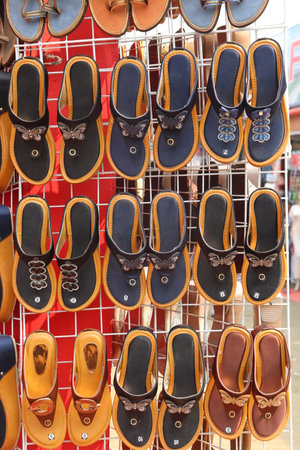 Rack showcases an array of sandals in brown, blue, and black hues. The sandals are designed with butterfly adornments. Footwear on display.の写真素材