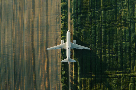 Aerial view of a passenger plane flying over the green fieldの素材