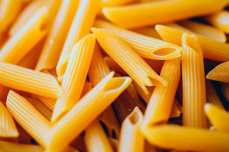 This photograph showcases a detailed close-up of penne pasta. Highlighted is the pasta's golden hue and ribbed texture.の素材