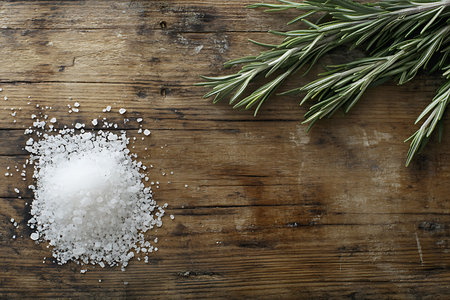 Top-down shot shows fresh rosemary sprigs and a pile of coarse sea salt on a weathered wooden surface, ideal for culinary or ingredient-focused designs.の素材