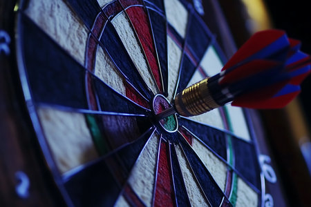A focused close-up highlights a dart accurately striking the bullseye on a sharp, colorful dartboard, signaling a successful game achievement.の素材