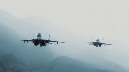 Low-angle view shows two Mig-29 fighter jets flying in formation. The lead plane is closer, while the other follows behind against a blurred mountain backdrop.の素材