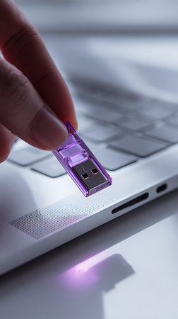 Close-up photo depicts a hand inserting a transparent purple USB drive into a laptop. Focus highlights data transfer, technology, and digital storage solutions.の素材