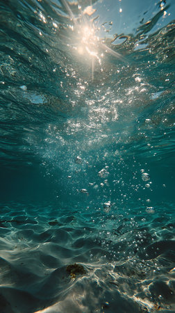 Glimpse beneath the waves, where sunlight dances through the turquoise water and illuminates the sandy seabed. Bubbles ascend towards the surface, creating a mesmerizing underwater scene.の素材