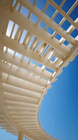 Upward view of the intricate white wooden beams of a pergola. The structure curves elegantly against a bright blue sky, creating contrast and emphasizing architectural detail.の素材