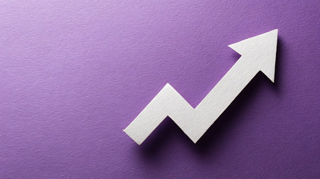 A white paper arrow with an upward trend rests on a textured purple background. The arrow zigzags upwards, indicating growth or positive direction on a textured surface.の素材