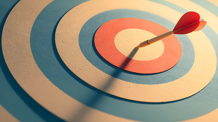 Close-up of an arrow perfectly hitting the bullseye on a target. The target has concentric circles of blue, beige, and orange, creating a visually appealing design.の素材