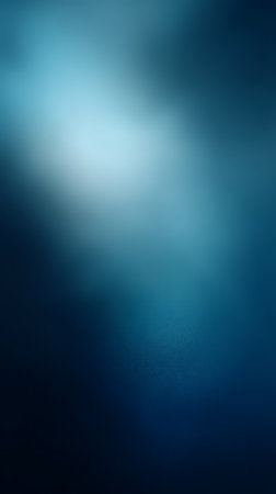 Abstract blue gradient background featuring a soft, diffused light spot in the upper region. The color ranges from light cyan to navy creating depth.の素材