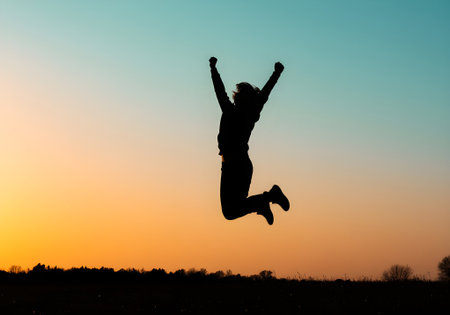 Silhouette of a woman jumping in the air at sunset.の素材