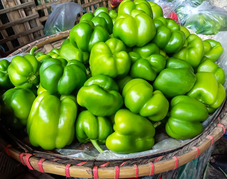 A bountiful harvest of vibrant green bell peppers is artfully arranged in a rustic woven basket, ready for market.の写真素材