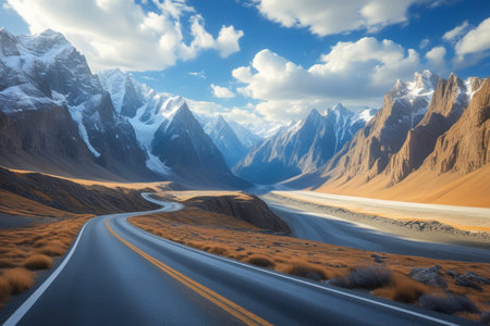 A scenic asphalt road curves through a vast mountain valley with snow-capped peaks and dramatic rock formations under a bright, cloudy sky.の素材