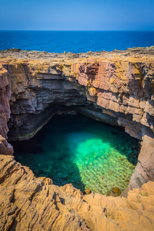 A vibrant turquoise pool within a rocky sea cave, illuminated by sunlight, with the blue ocean in the background.の素材