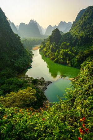 A serene river winds through a valley of dramatic karst mountains, shrouded in soft morning mist and vibrant green foliage.の素材
