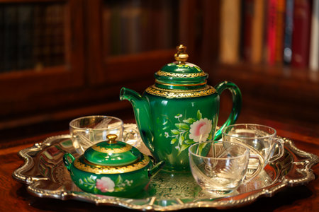 A beautifully ornate green teapot, sugar bowl, and delicate cups are presented on a decorative silver tray.の素材