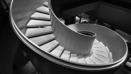 A striking monochrome image of a modern spiral staircase, showcasing its geometric curves and clean lines.の素材