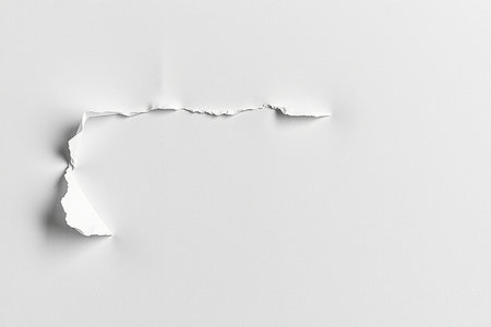 A close-up of a white surface with a torn section revealing a rough, ragged edge and a hint of shadow. Minimalist abstract.の素材