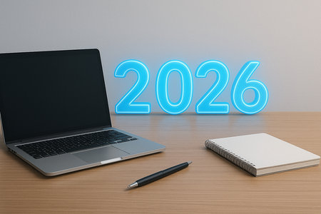 A modern laptop, pen, and book sit on a wooden desk with a glowing 2026 sign.の素材