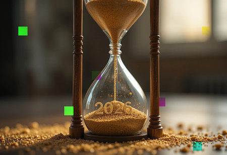 An antique hourglass with sand flowing through, set against a blurred background.の素材