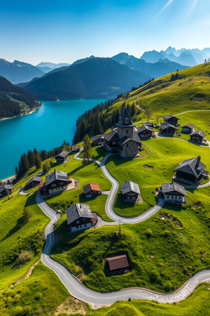 An aerial view of a charming Swiss village with winding roads, green hills, and a vibrant blue lake.の素材