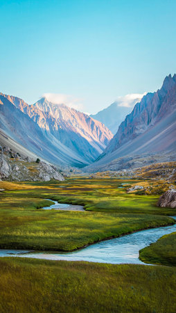 Serene mountain valley with a winding river and lush green fields under a clear blue sky.の素材