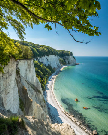 A stunning coastal landscape featuring dramatic white cliffs, a sandy beach, and clear blue-green water, framed by vibrant green tree branches.の素材