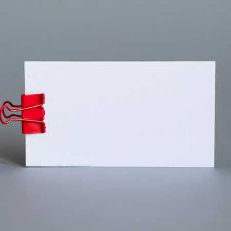 Blank white business card held by a vibrant red binder clip on a neutral gray surfaceの素材