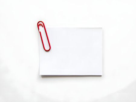 A single red paperclip secures a blank white note card on a clean white backgroundの素材
