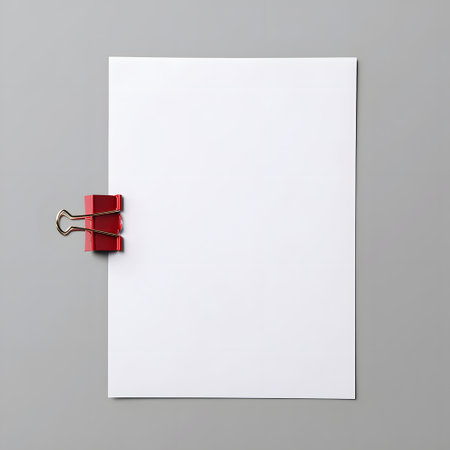Blank white paper sheet held by a bright red binder clip on a neutral gray backgroundの素材